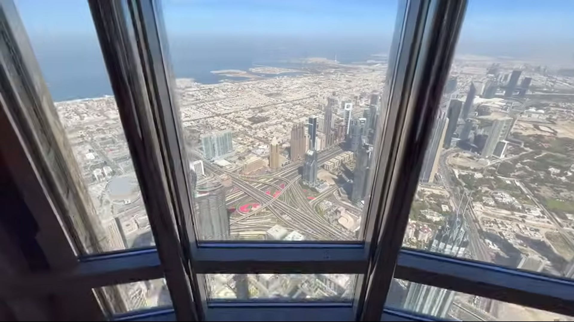 Aerial view from Burj Khalifa windows over Dubai highways, towers, and coastline